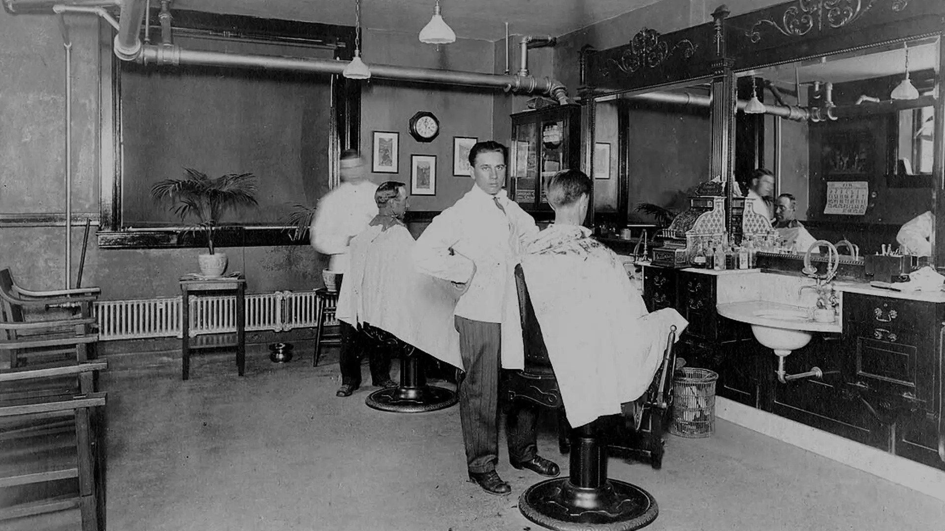 Barberos atendiendo a clientes en una barbería de archivo de 1920