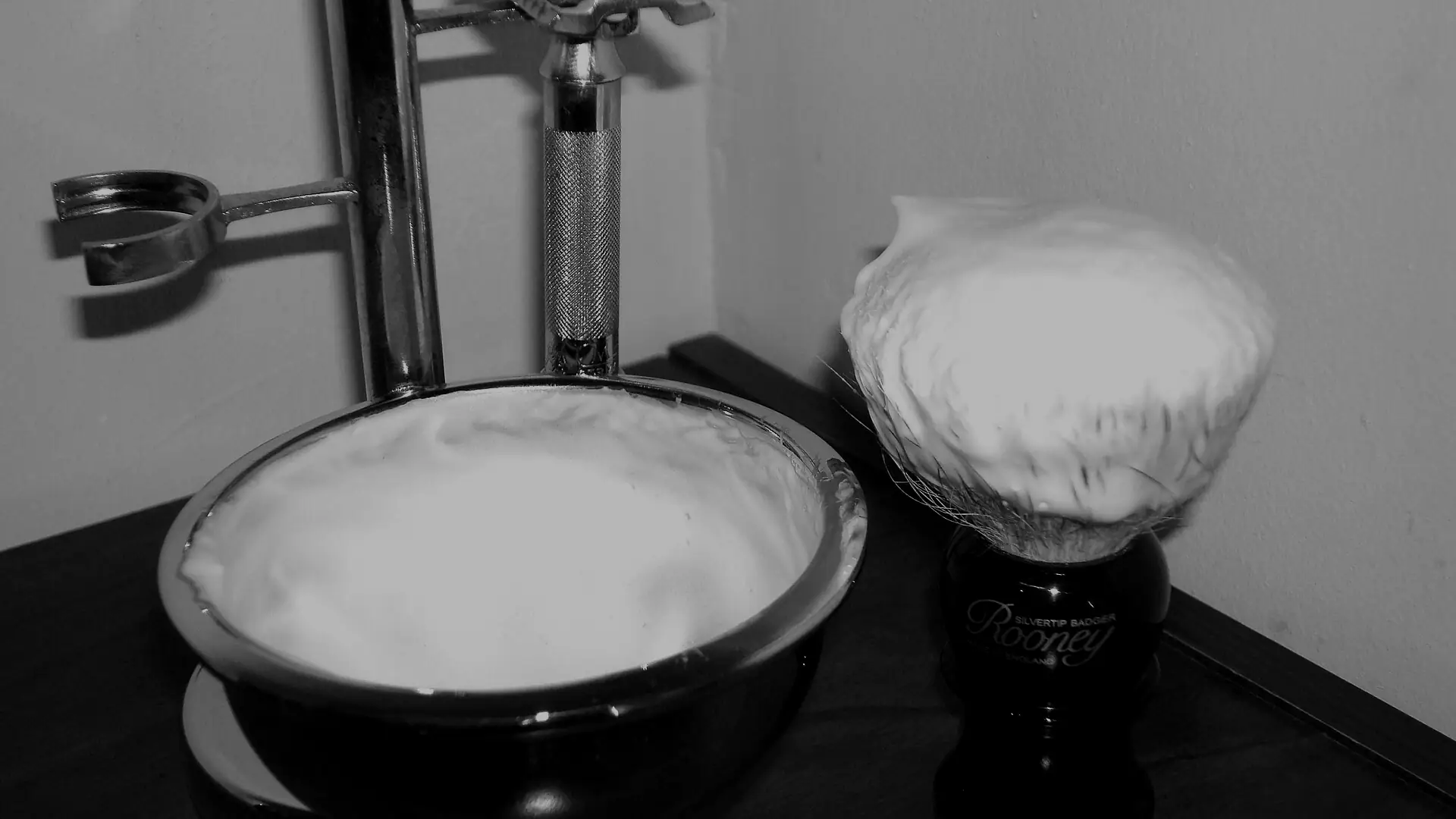 Brocha de afeitar con espuma junto a un bol y una maquinilla